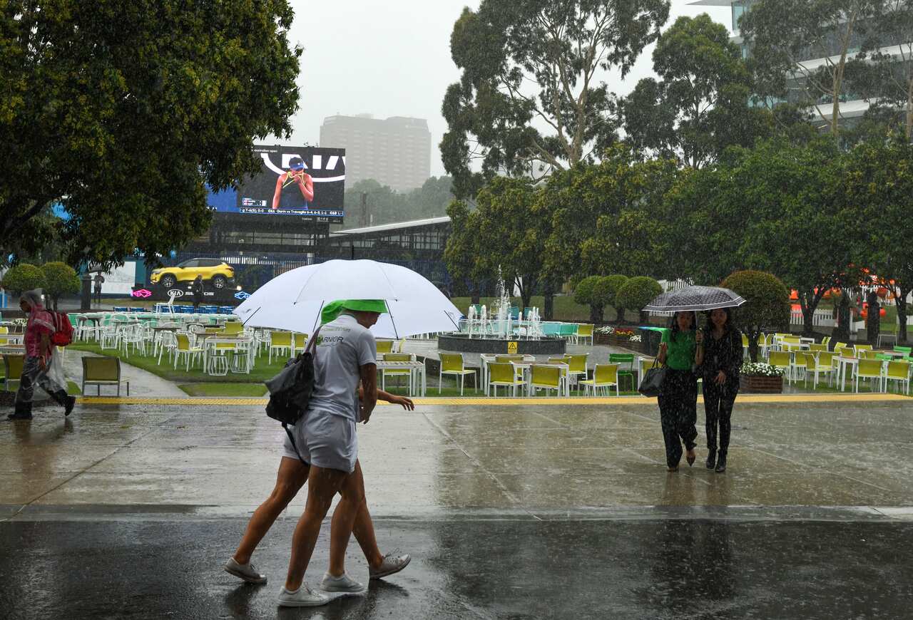 Spectators are seen as rain falls during the first round matches during day one of the Australian Open tennis tournament in Melbourne.