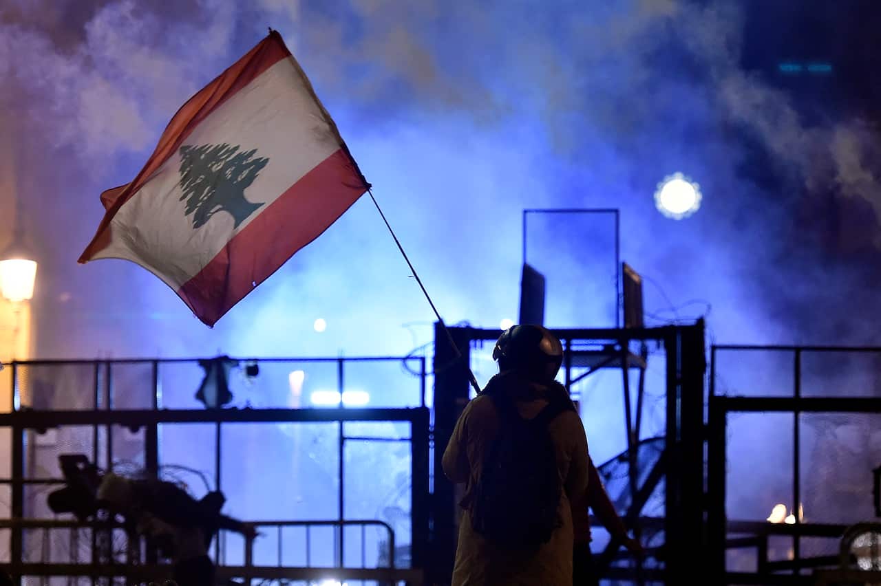 An anti-government protester waves a Lebanese flag during protests and clashes with police outside the Lebanese Parliament building.
