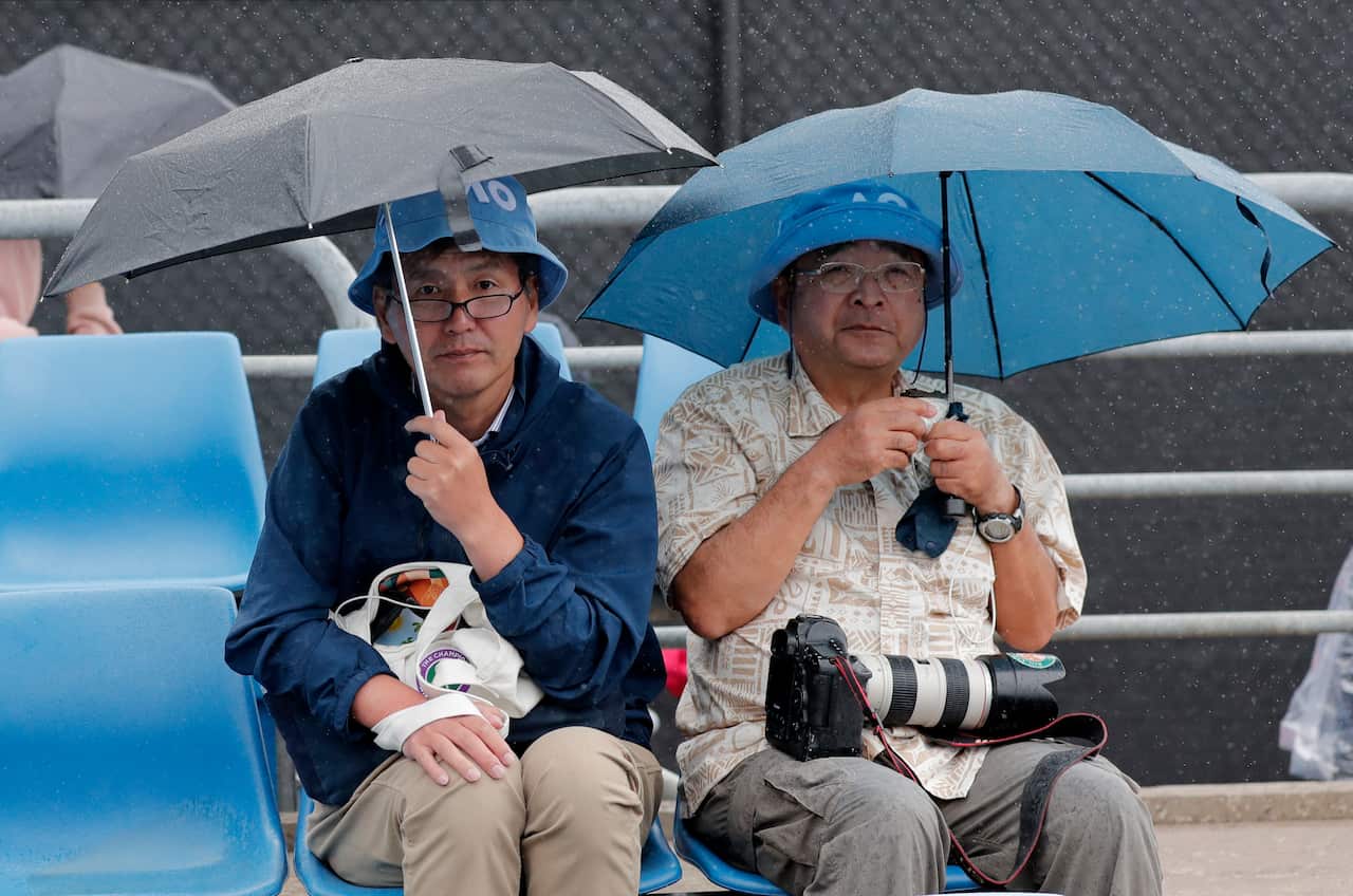 Spectators sit in the rain as play is halted during a second round singles matches at the Australian Open tennis championship in Melbourne.