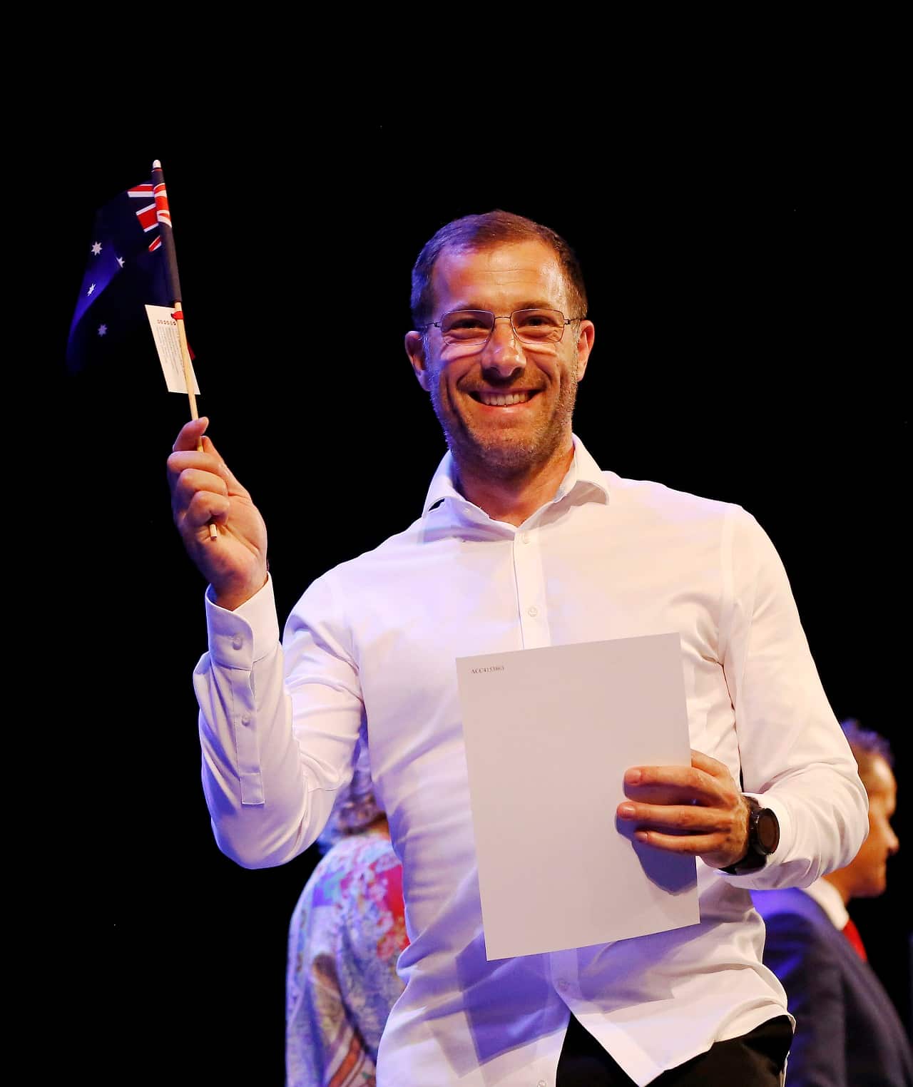 New Australian Sylvain Della Libera waves his the Australian flag at a citizenship ceremony.