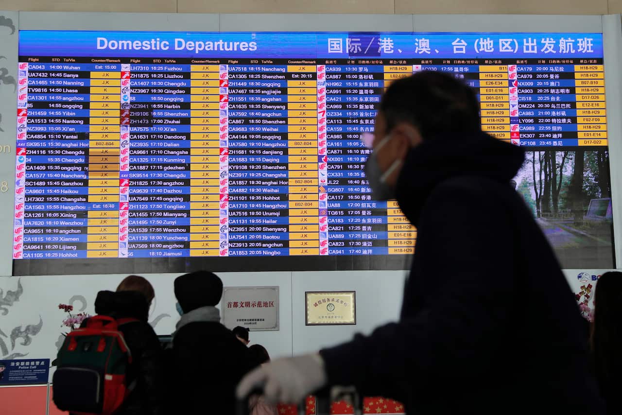 A passenger wears a mask passing by a departure information screen at Beijing Capital International Airport