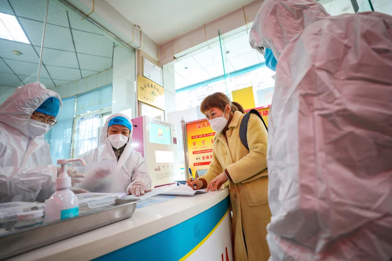 Medical workers in protective gear talk with a woman suspected of being ill with coronavirus at a community health station in Wuhan.