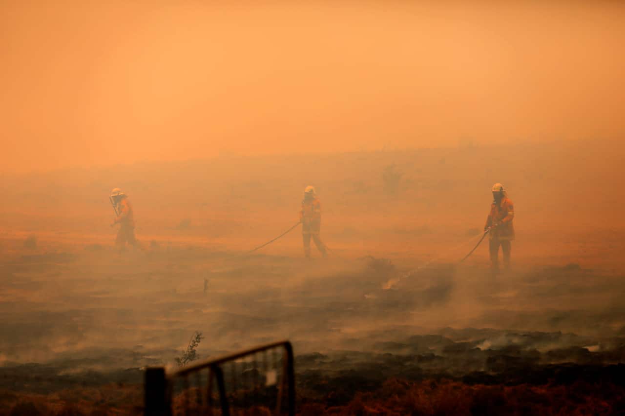 NSW Rural Fire Service crews appear barely distinguishable amid haze after extinguishing a fire that crossed the Monaro Highway, four km north of Bredbo.