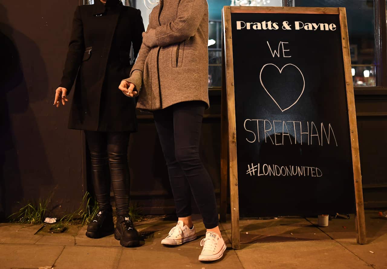 People smoke cigarettes next to a sign outside a bar in Streatham, London.