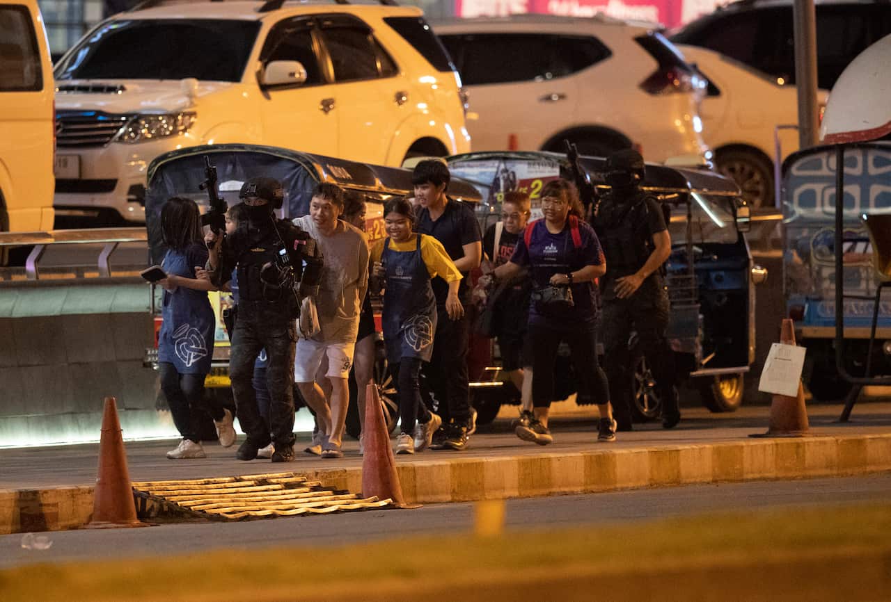 People who were able to get out of Terminal 21 Korat mall are escorted outside by armed commando soldiers.