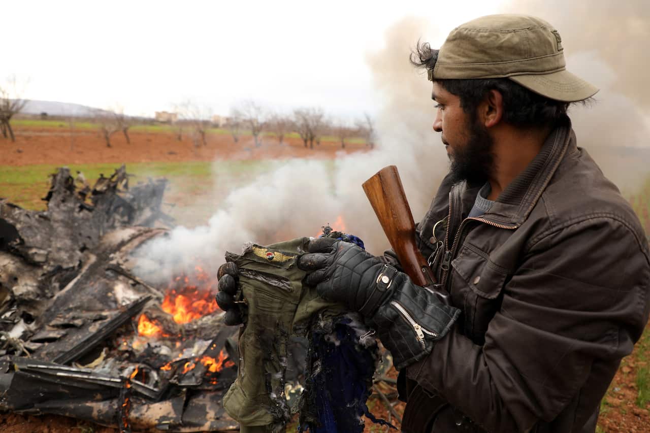An armed man shows belongings of a pilot who was on an alleged Syrian army helicopter that was shot down in the village of Qaminas.