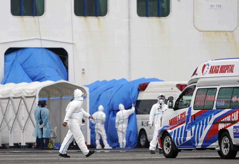 Personnel in protective gear walk towards the Diamond Princess cruise ship docked at the Daikoku Pier Cruise Terminal