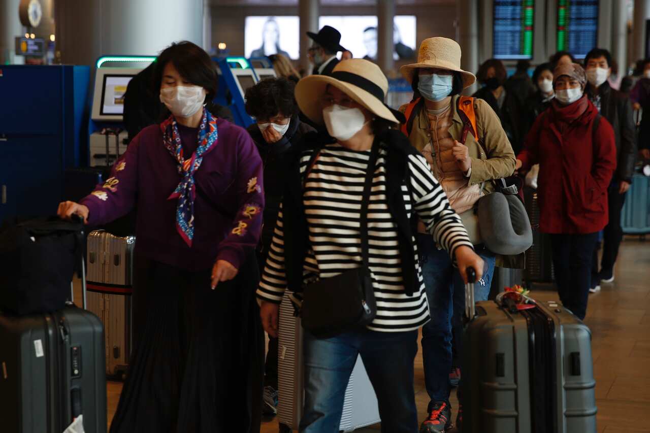 Tourists from Korea wear protective masks as they walk with their belongings at the Ben Gurion Airport near Tel Aviv, Israel, Sunday, Feb. 23, 2020. (AP Photo/Ariel Schalit)