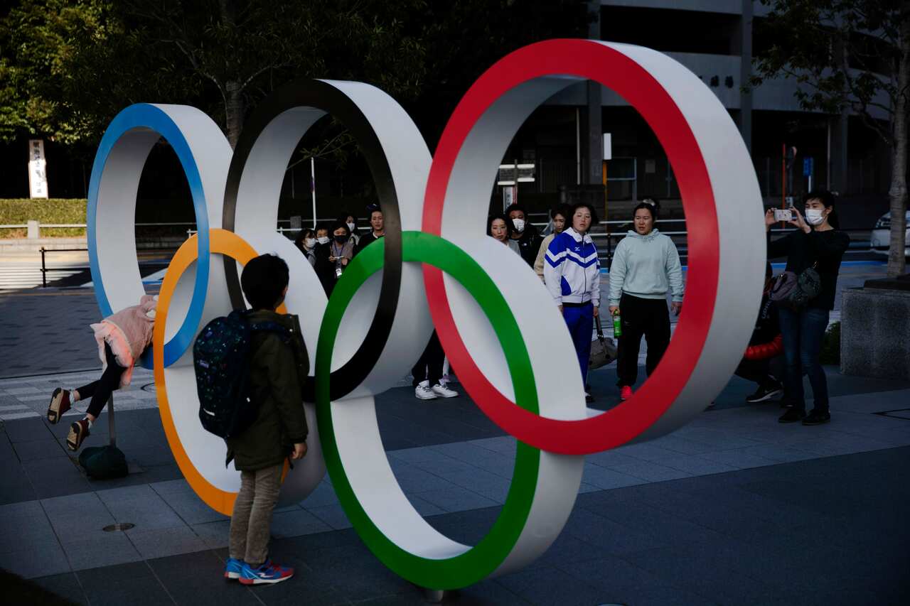 People wait in line to take pictures with the Olympic rings near the New National Stadium in Tokyo.