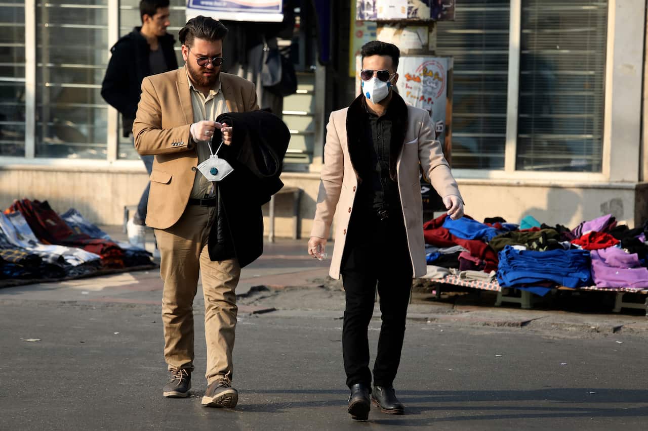 Pedestrians cross a street as one of them prepares his face mask in western Tehran, Iran, Saturday, 29 February, 2020.