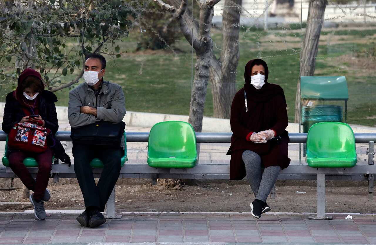 People wearing face masks wait for bus in a bus stop in a street in western Tehran, Iran.