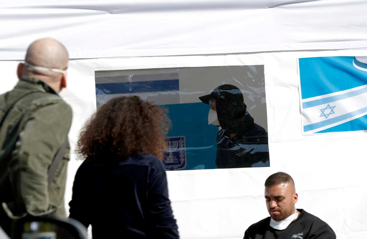Israelis watch a woman casting her ballot inside a special polling station for voters in home quarantine on coronavirus suspicion, in Tel Aviv, Israel.