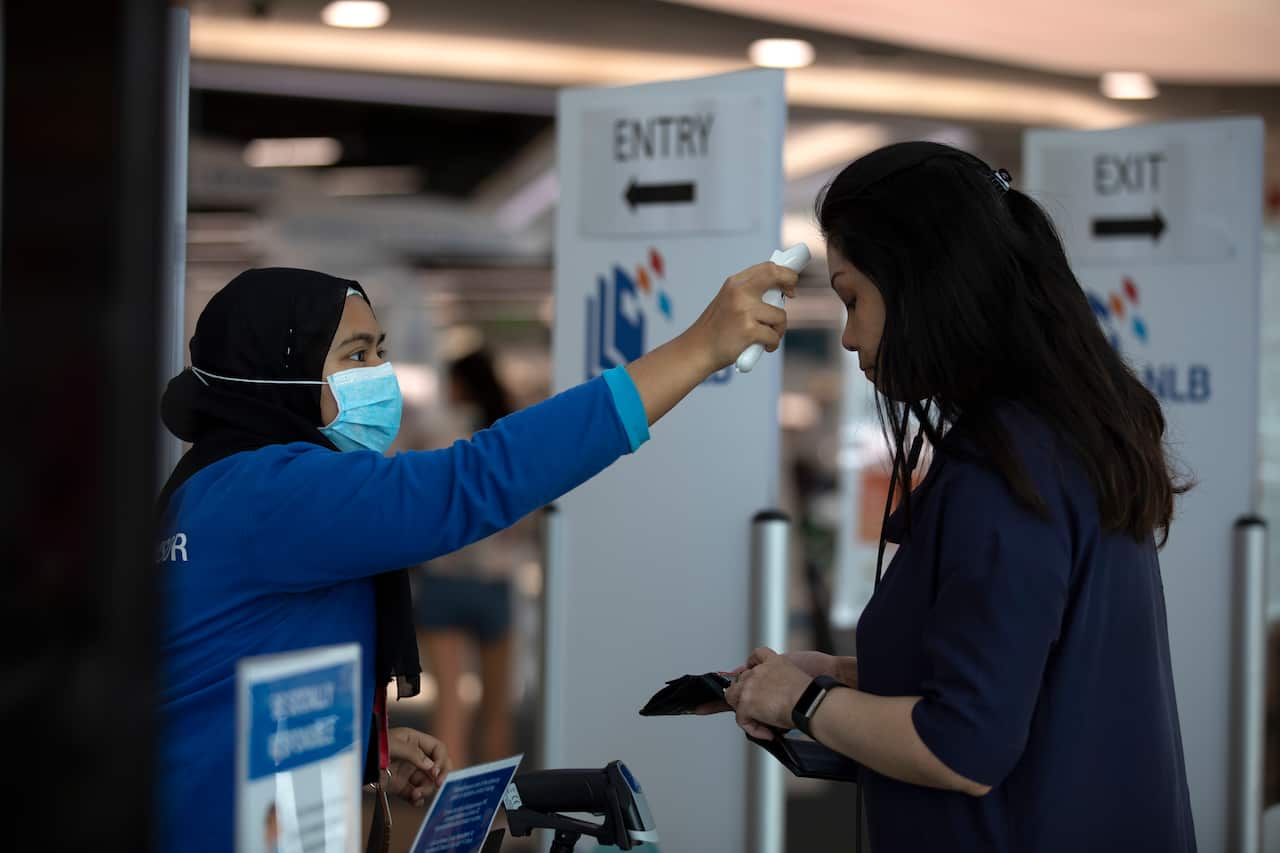 A staff takes the temperature of a visitor at the entrance of a library in Singapore.