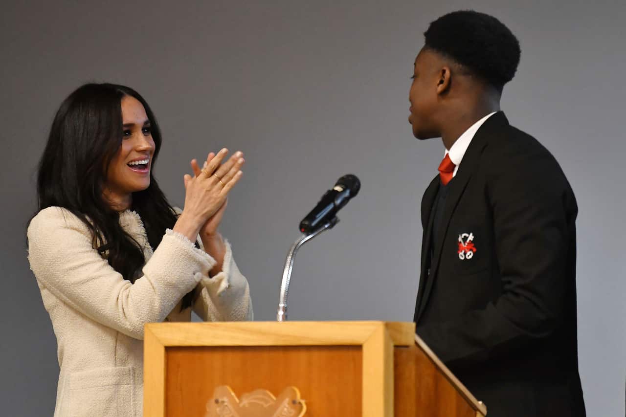 The Duchess of Sussex (left) smiles as head boy Aker Okoye, speaks in a school assembly.