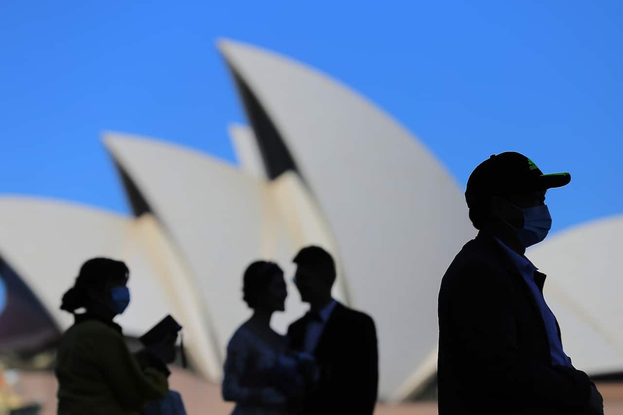 People wear face masks in front of the Sydney Opera House.
