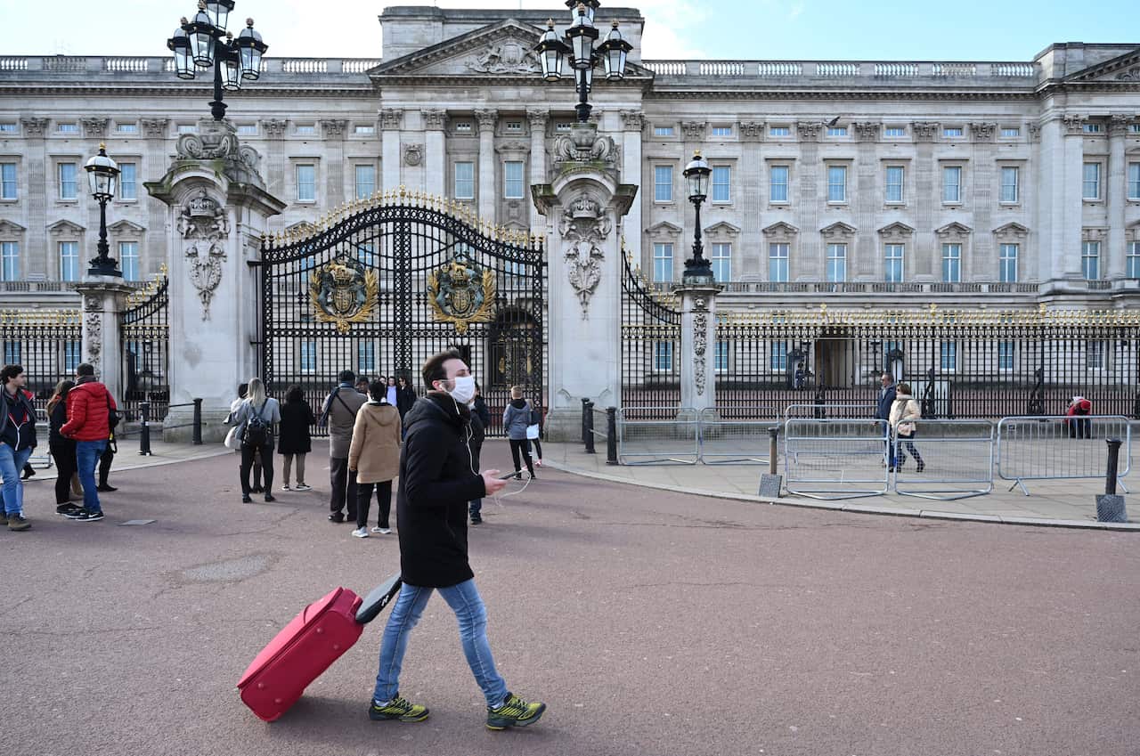 A man in a surgical mask passes an unusually small crowd outside Buckingham Palace in London, Britain.