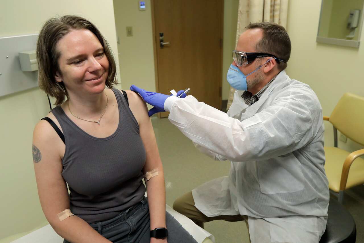 Jennifer Haller, left, smiles as she s given the first shot in the safety study clinical trial of a potential vaccine for the coronavirus in Washington.