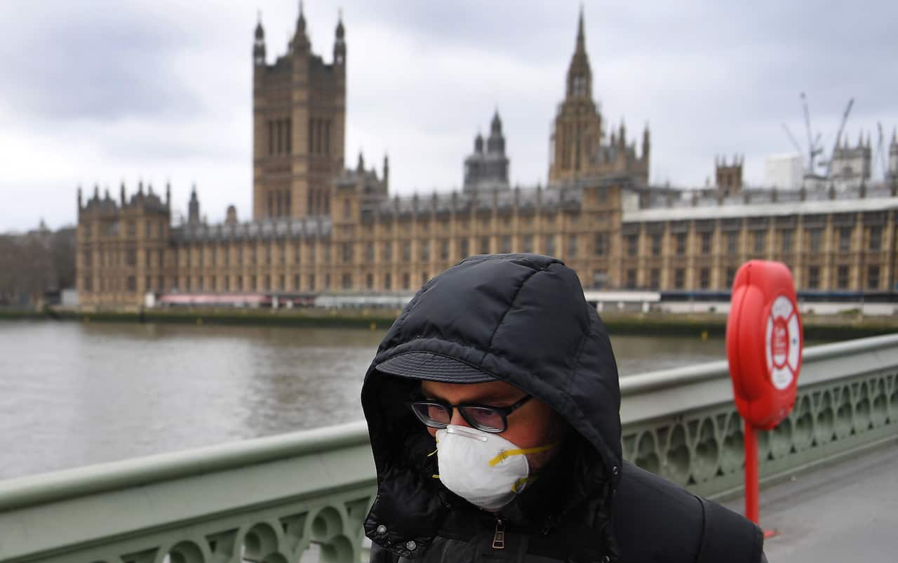  A man wearing a protective face mask walks past Westminster Palace parliament in London, Britain, 18 March 2020. 