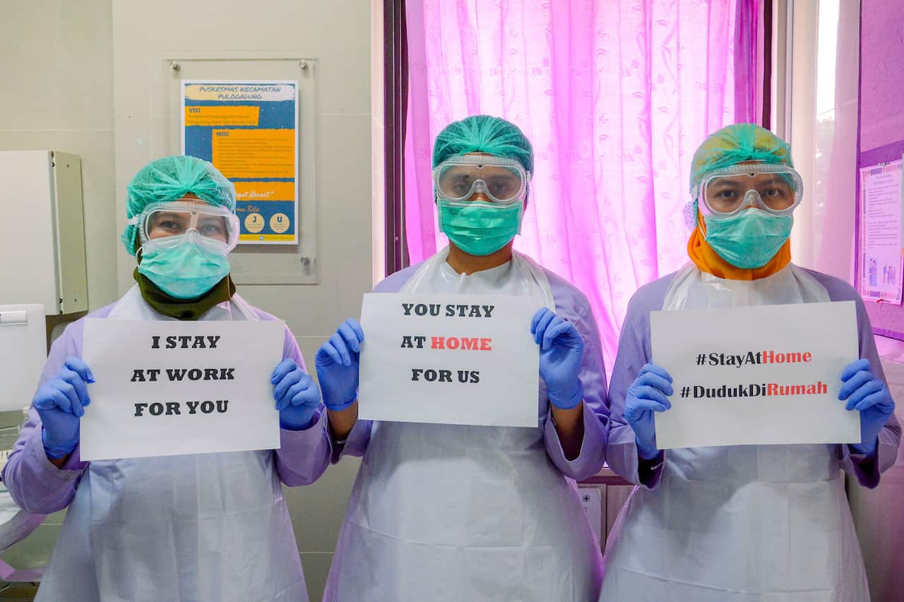 Medical workers wearing a face mask holds a 'Stay at Home' poster at a medical center in Jakarta, Indonesia.