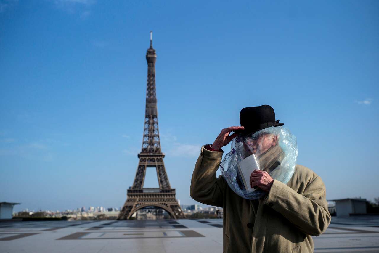 A man covered with plastic bag for protection reads a book in front of the Eiffel tower in Paris, France