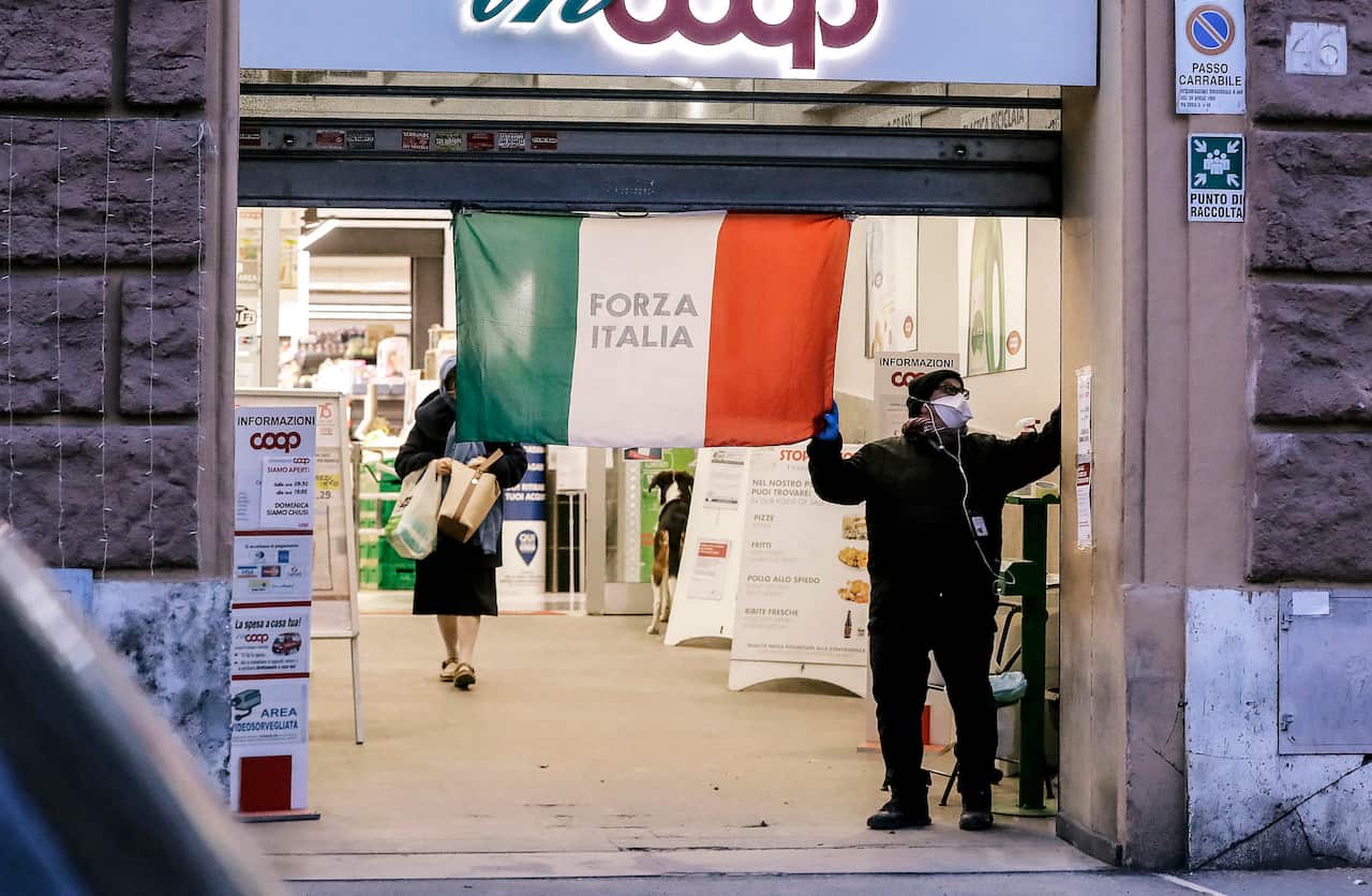 A man closes the shutter of a supermarket with an Italian Tricolor flag in Rome, Italy.