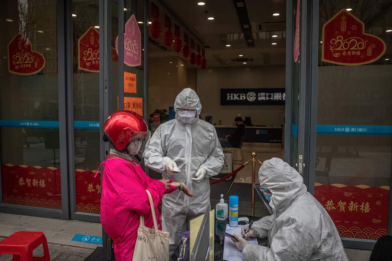 A worker in a protective outfit checks the body temperature of a woman at the entrance of a bank in Wuhan, China.