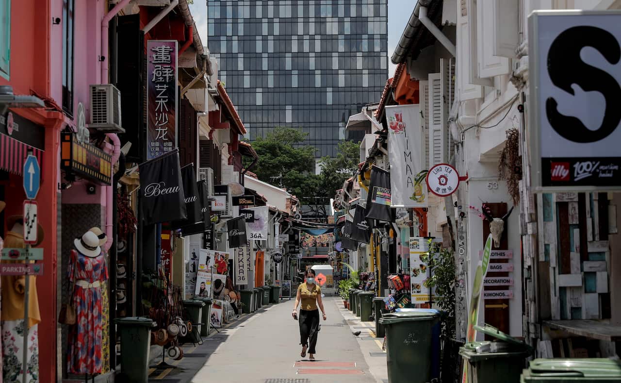 A young woman wearing a protective mask walks past shops in a deserted lane at Kampong Glam district in Singapore.