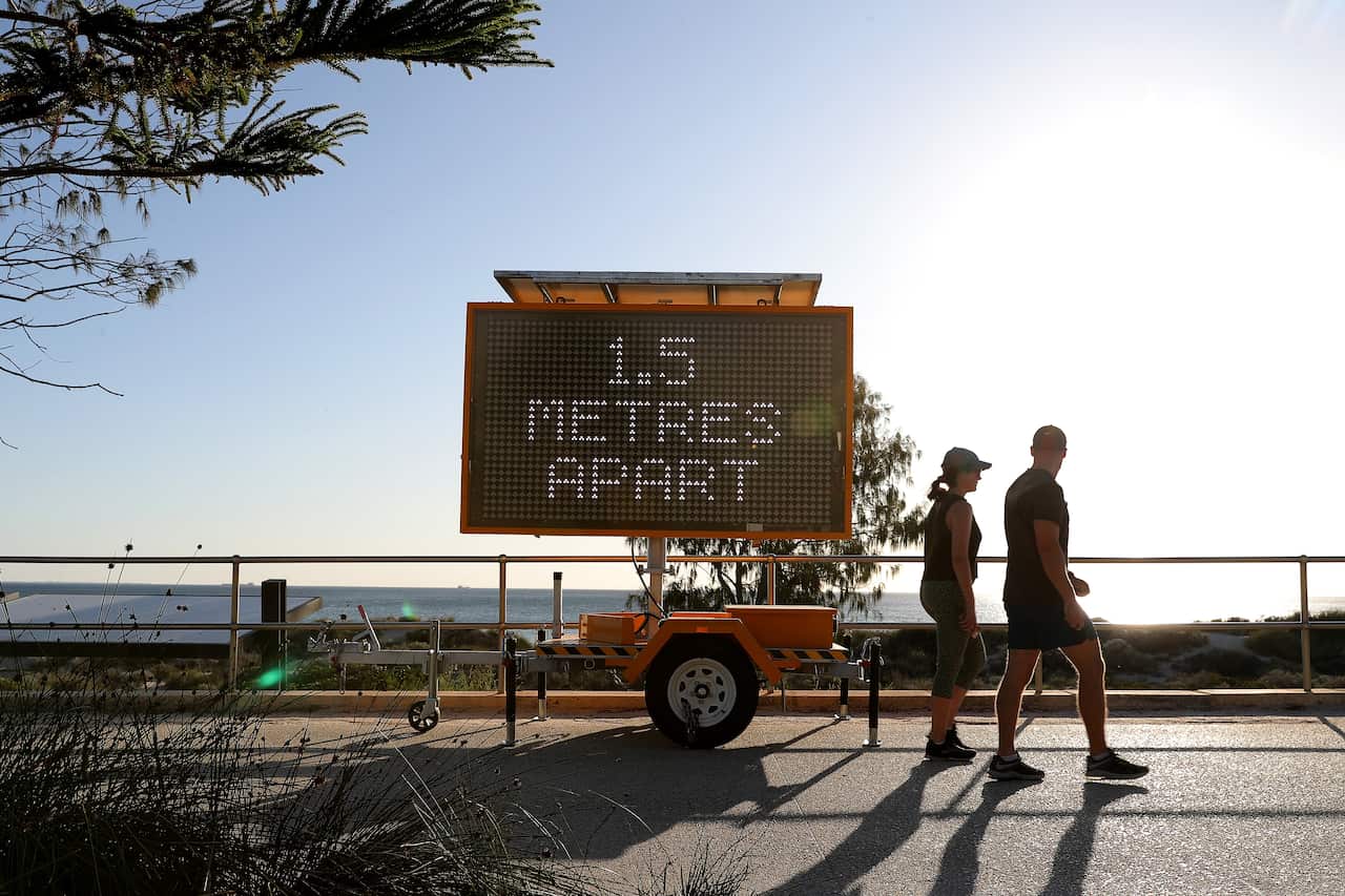 Members of the public are seen walking past a sign reading '1.5 metres apart' at Scarborough Beach, Perth.