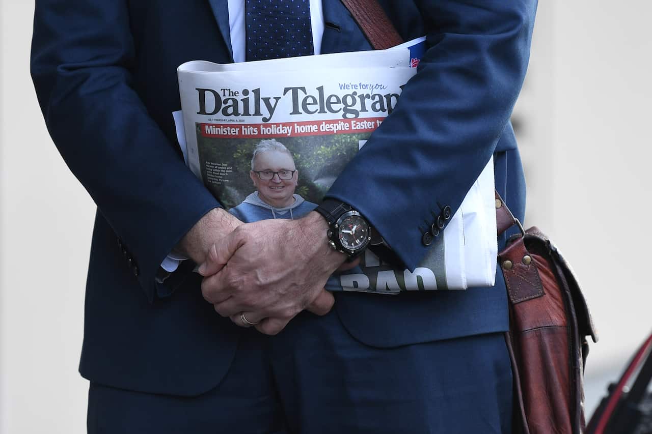A media adviser holds a newspaper cover featuring NSW Minister for the Arts Don Harwin.
