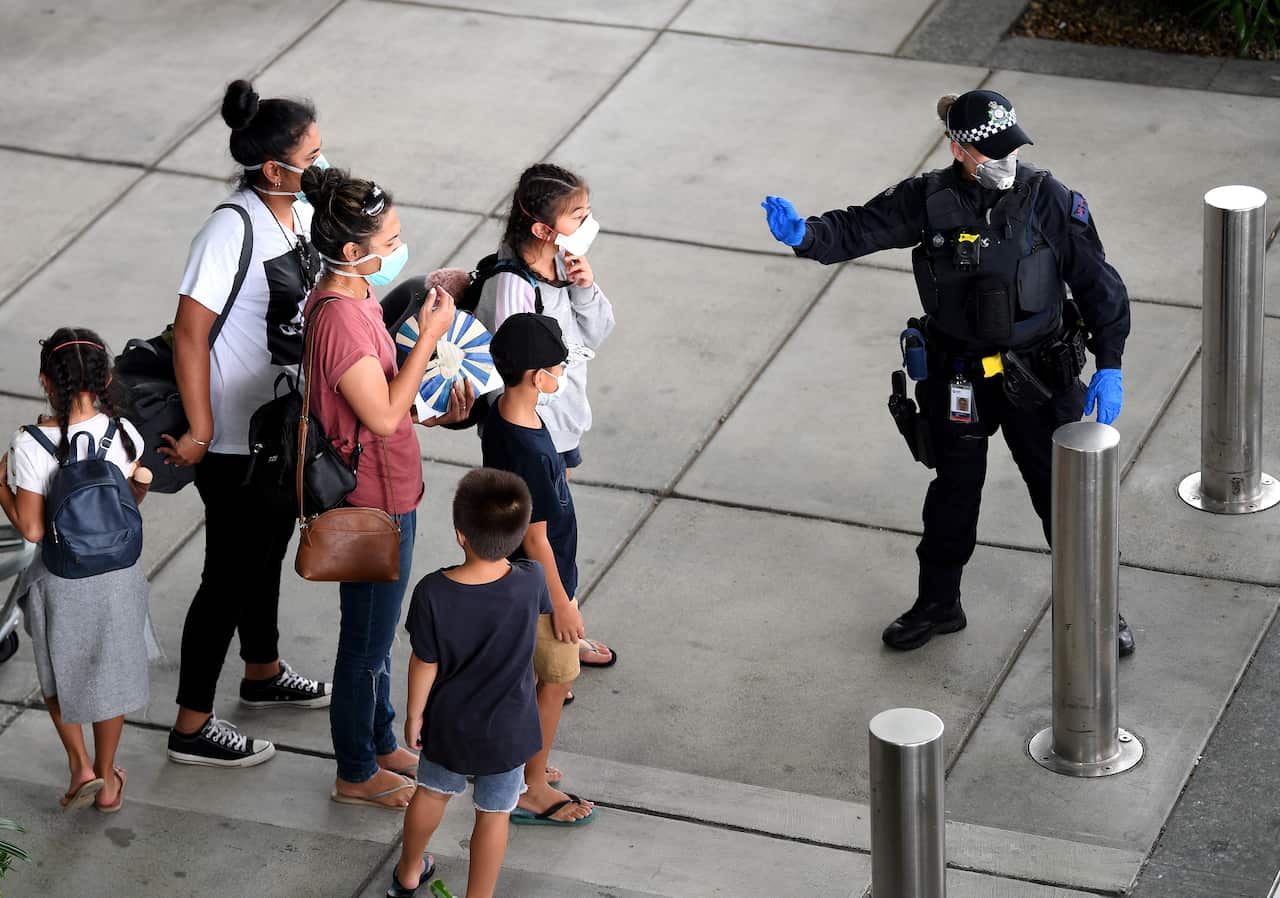 A police officer directs passengers who came on a special international repatriation flight as they arrive in Brisbane.