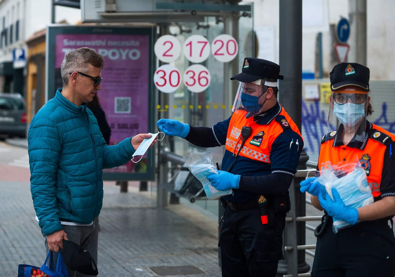 A member of Spanish Civil Protection gives a face masks to a citizen as a preventive measure against the spread of Covid-19 during lockdown.