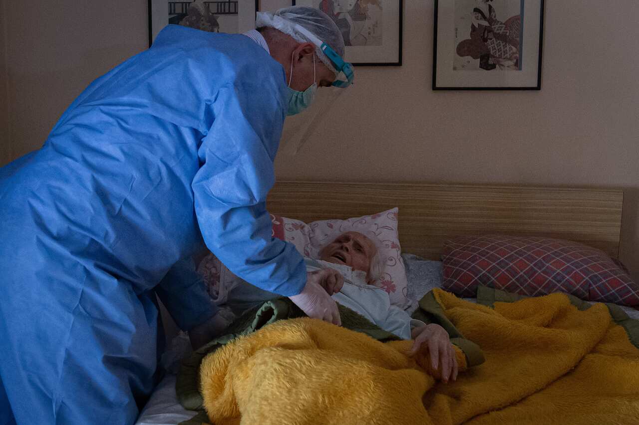 A doctor wearing protective gear stands next to an elderly woman.