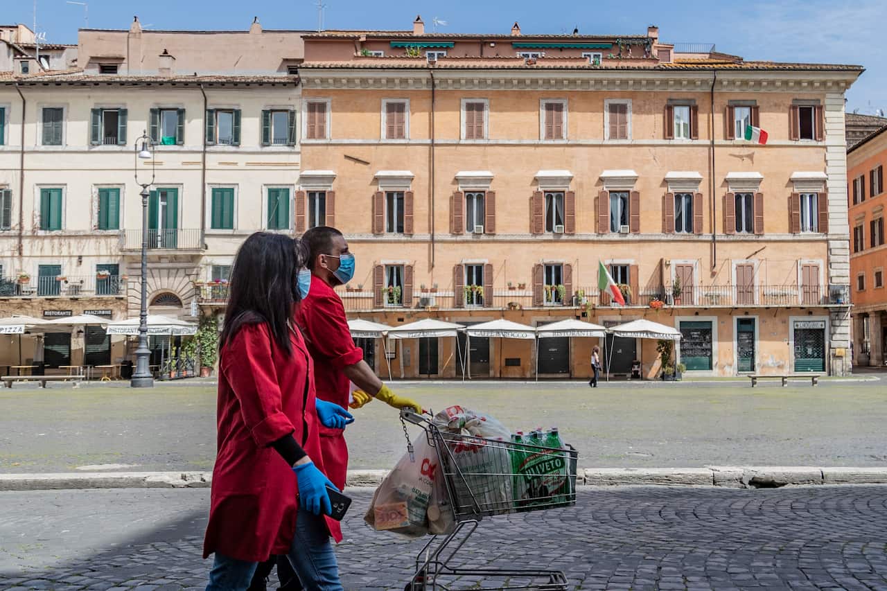 Two shop assistants bring grocery shopping in Piazza Navona empty square in Rome during the coronavirus emergency.