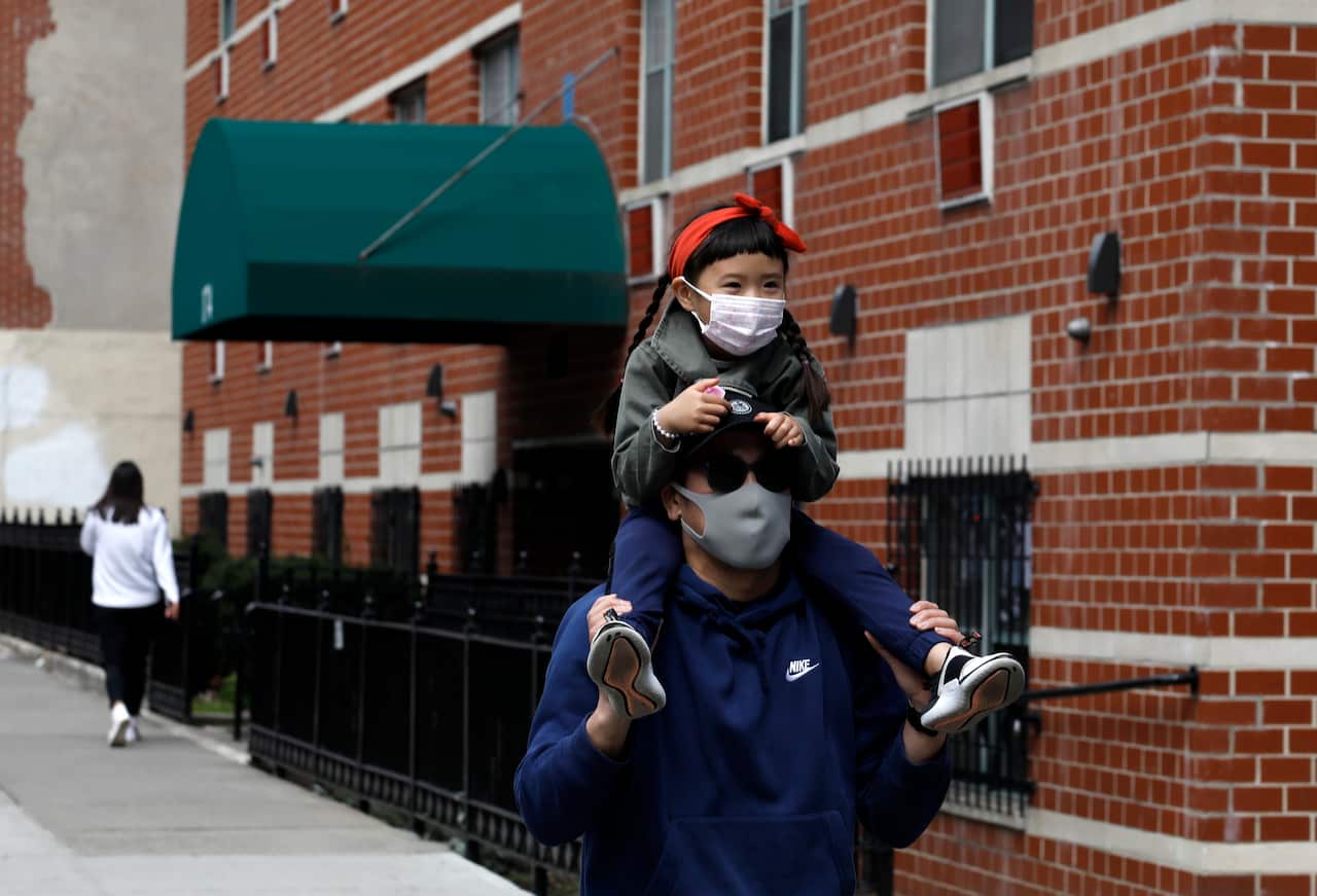 A child and her parent wear masks as they walk along the Alphabet City neighbourhood of New York.