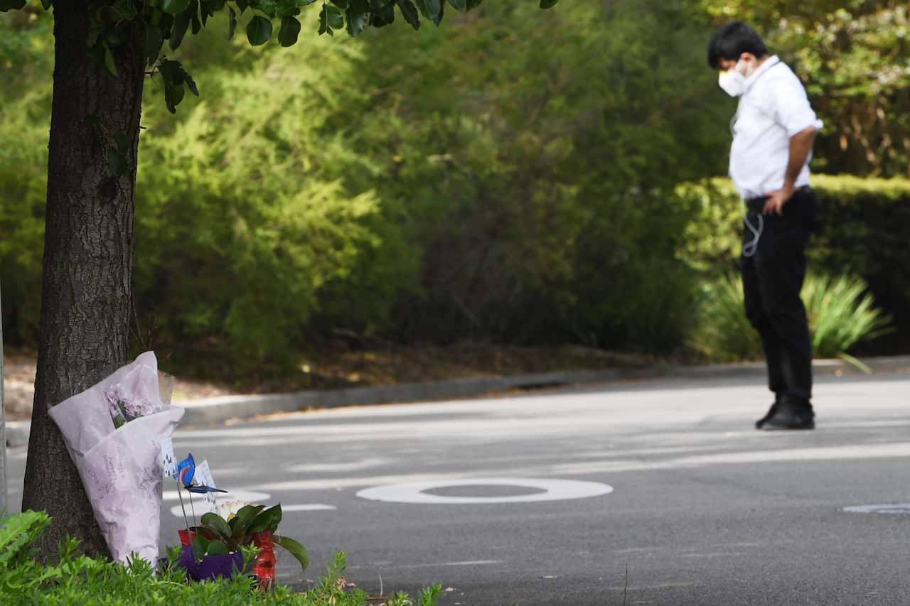 A security guard stands in the driveway as flowers are left at the entrance to Anglicare Newmarch House.