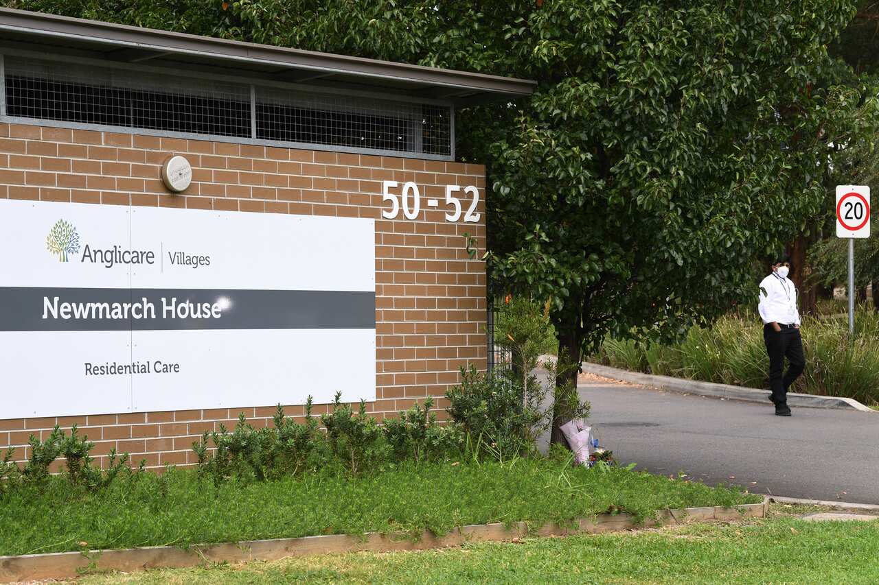 A security guard stands in the driveway as flowers are seen left at the entrance to Anglicare Newmarch House near Penrith.