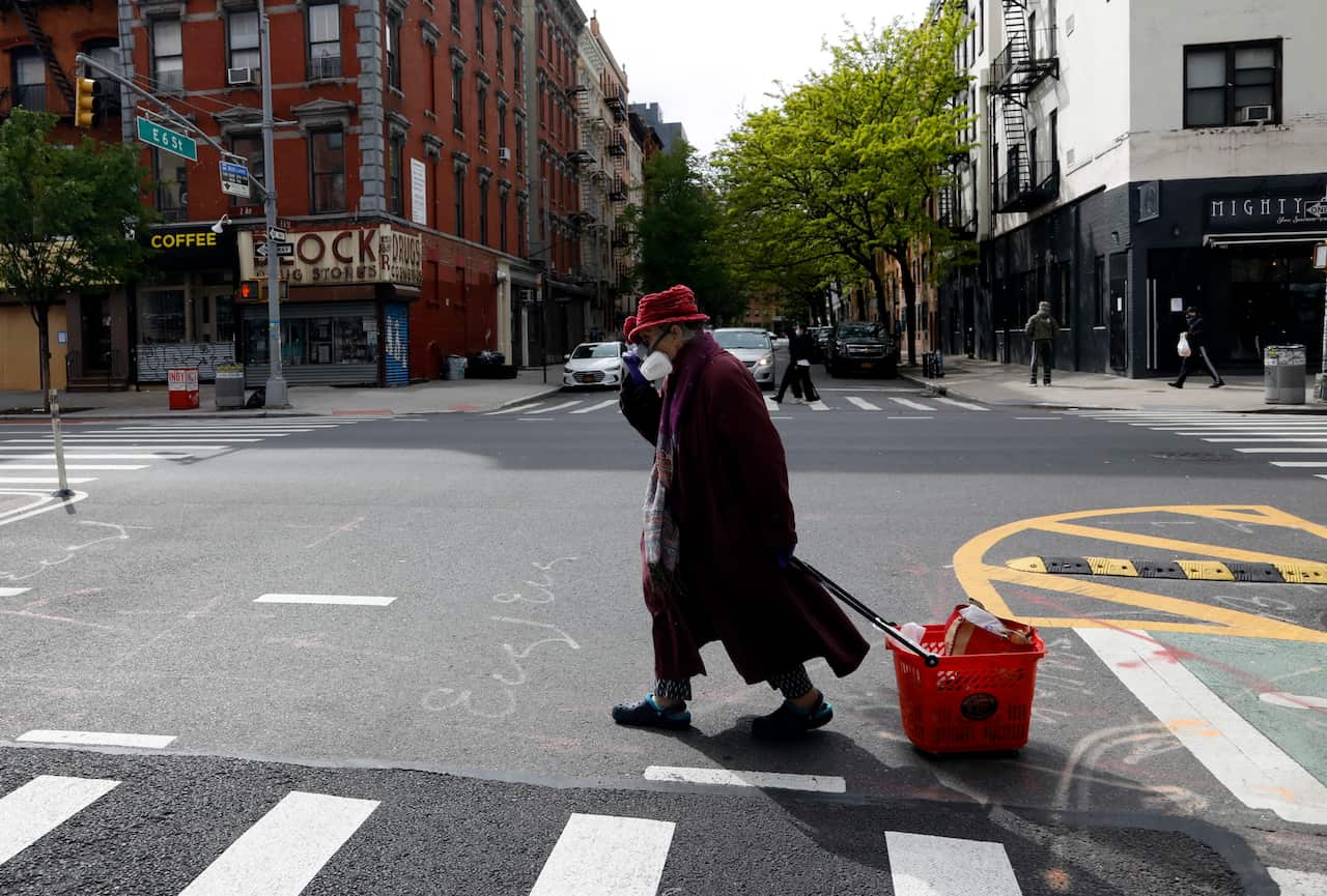  An elderly woman holds her hat as she wears a full face mask while crossing the street on the Lower East Side of New York. 