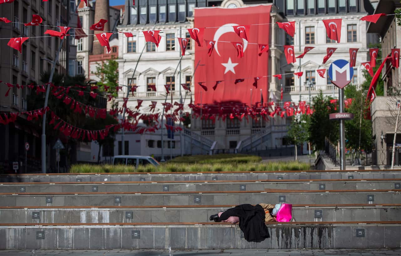 A homeless woman sleeps in front of the huge Turkish flag during a curfew amid the ongoing pandemic of COVID-19.