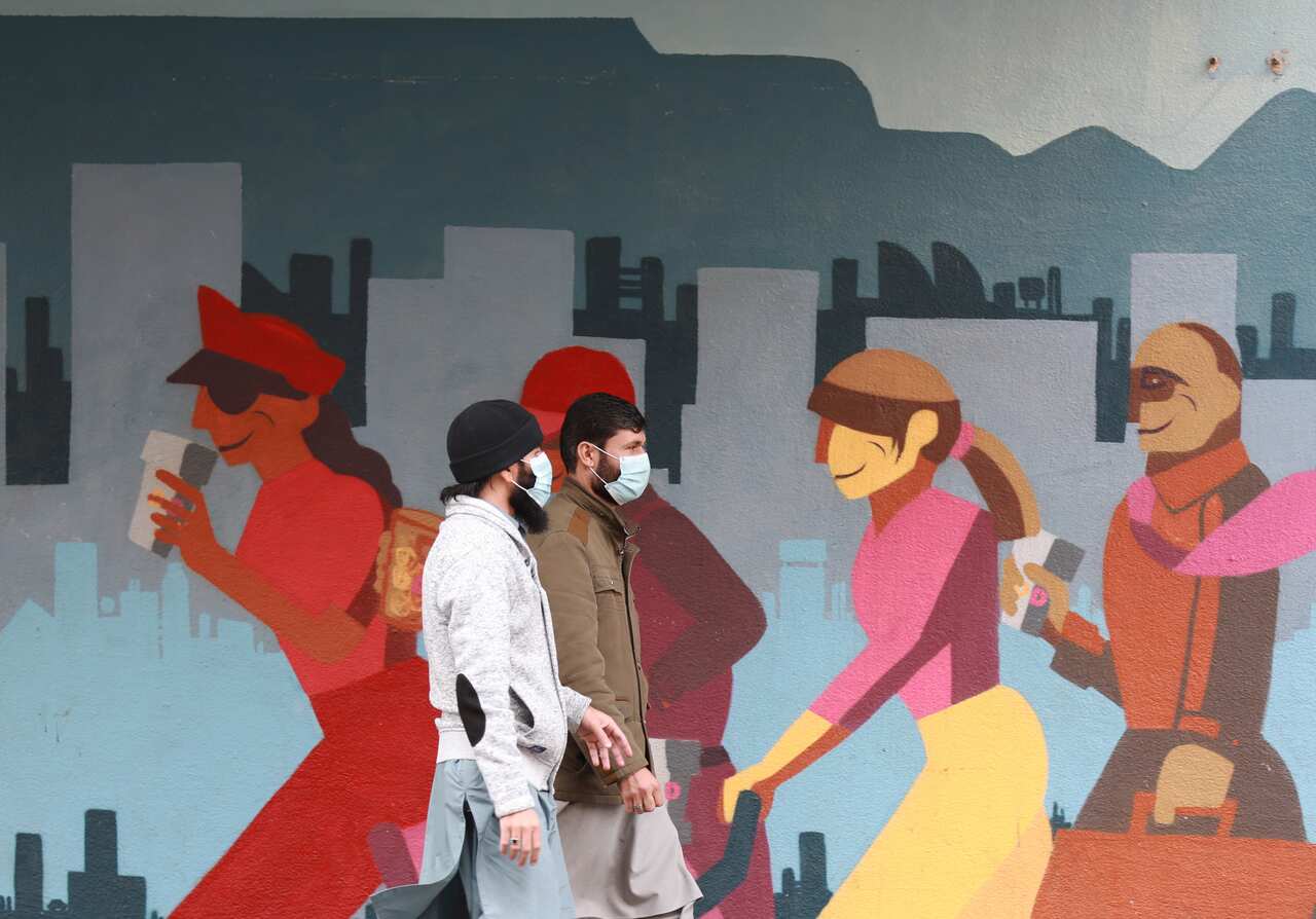 Men wearing face masks walk past a mural in Cape Town, South Africa.