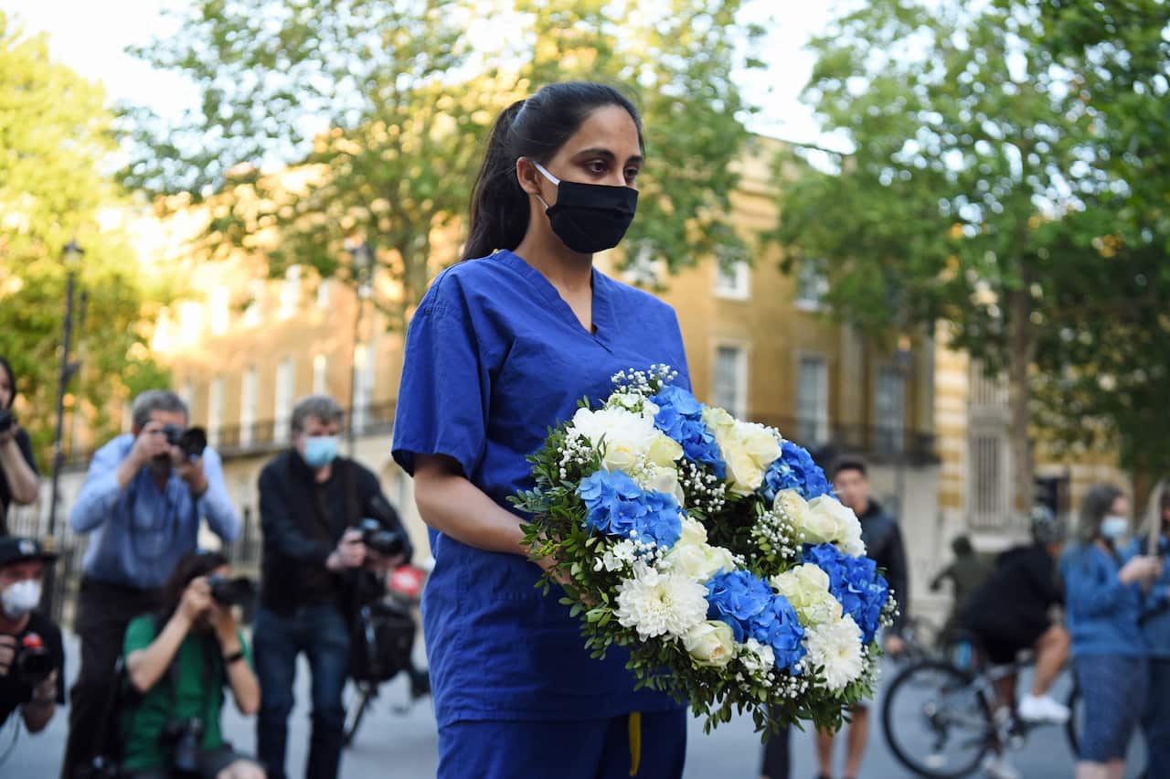 A woman wearing medical scrubs and a black mask carries a wreath of flowers in memory of people who have died during the coronavirus pandemic in the UK.