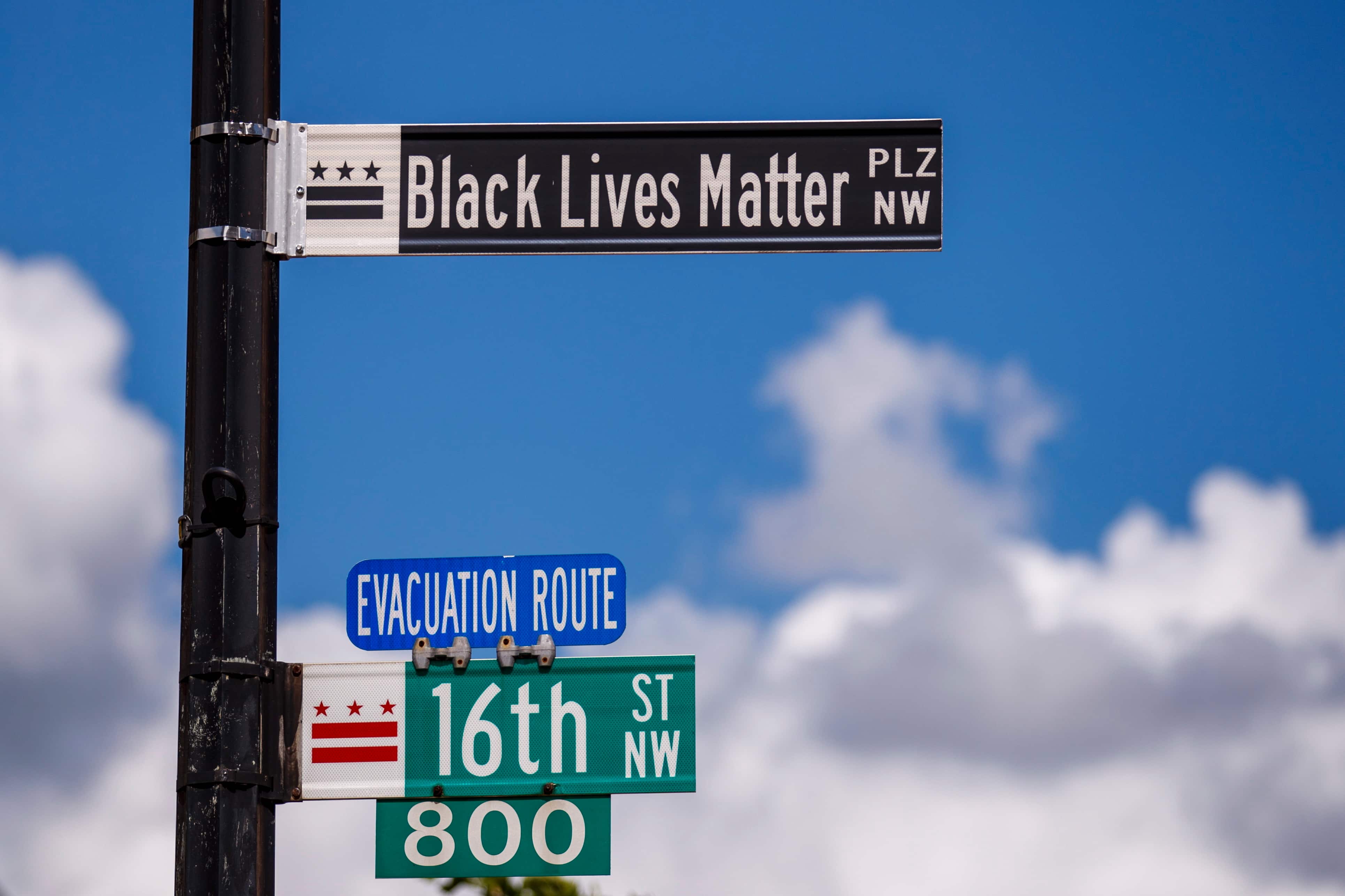 Street signs for 'Black Lives Matter PLZ NW' and '16th ST NW', with a blue sky background