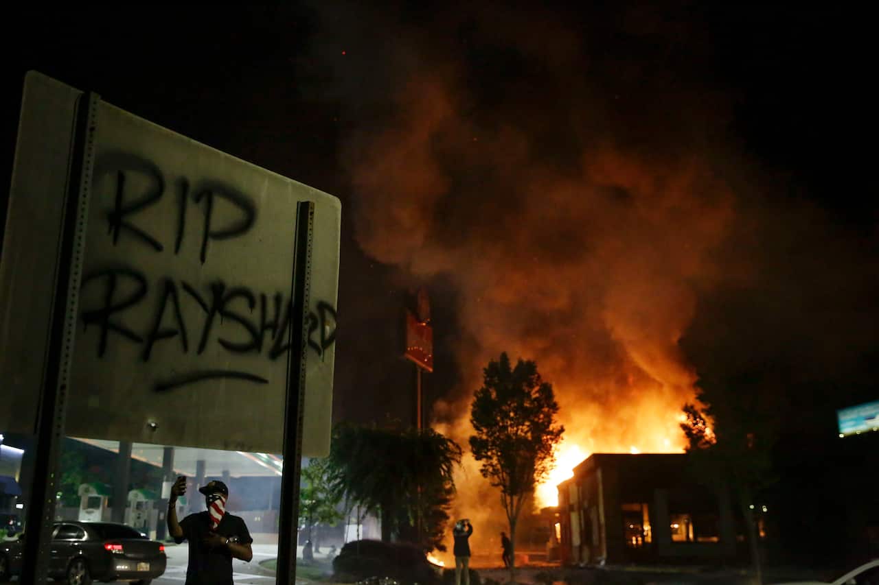 "RIP Rayshard" is spray painted on a sign as as flames engulf a Wendy's restaurant during protests.