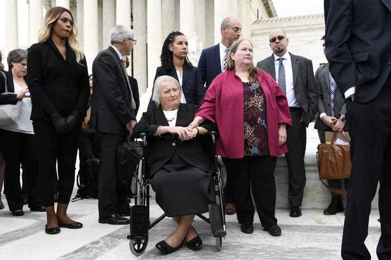 In this Oct. 8, 2019 file photo, Aimee Stephens, center, and her wife Donna Stephens, in pink, listen during a news conference outside the Supreme Court 