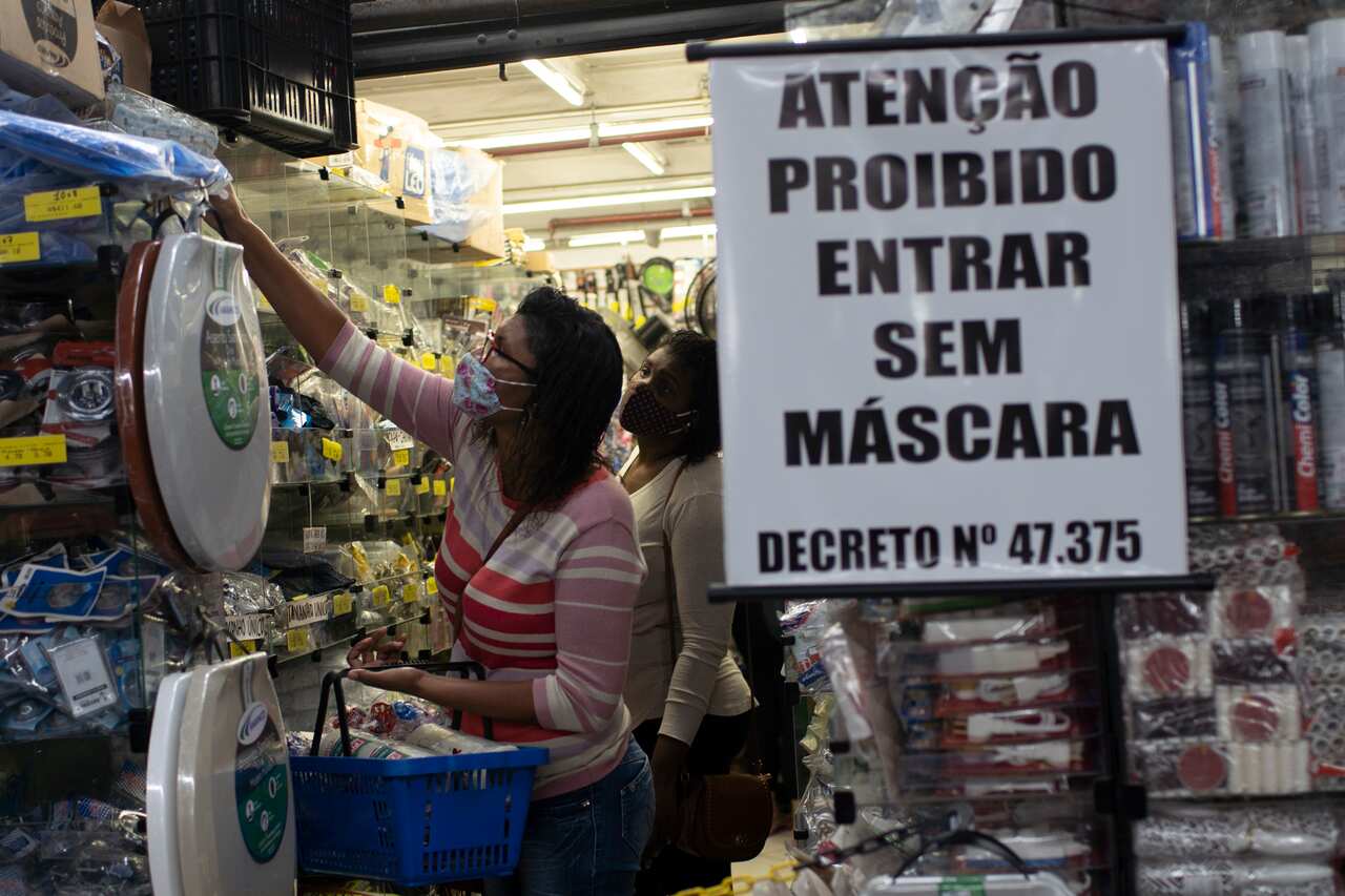 A shopper reaches for an item behind a sign that reads "Attention. Forbidden to enter without masks" at the Madureira Market in Rio. 