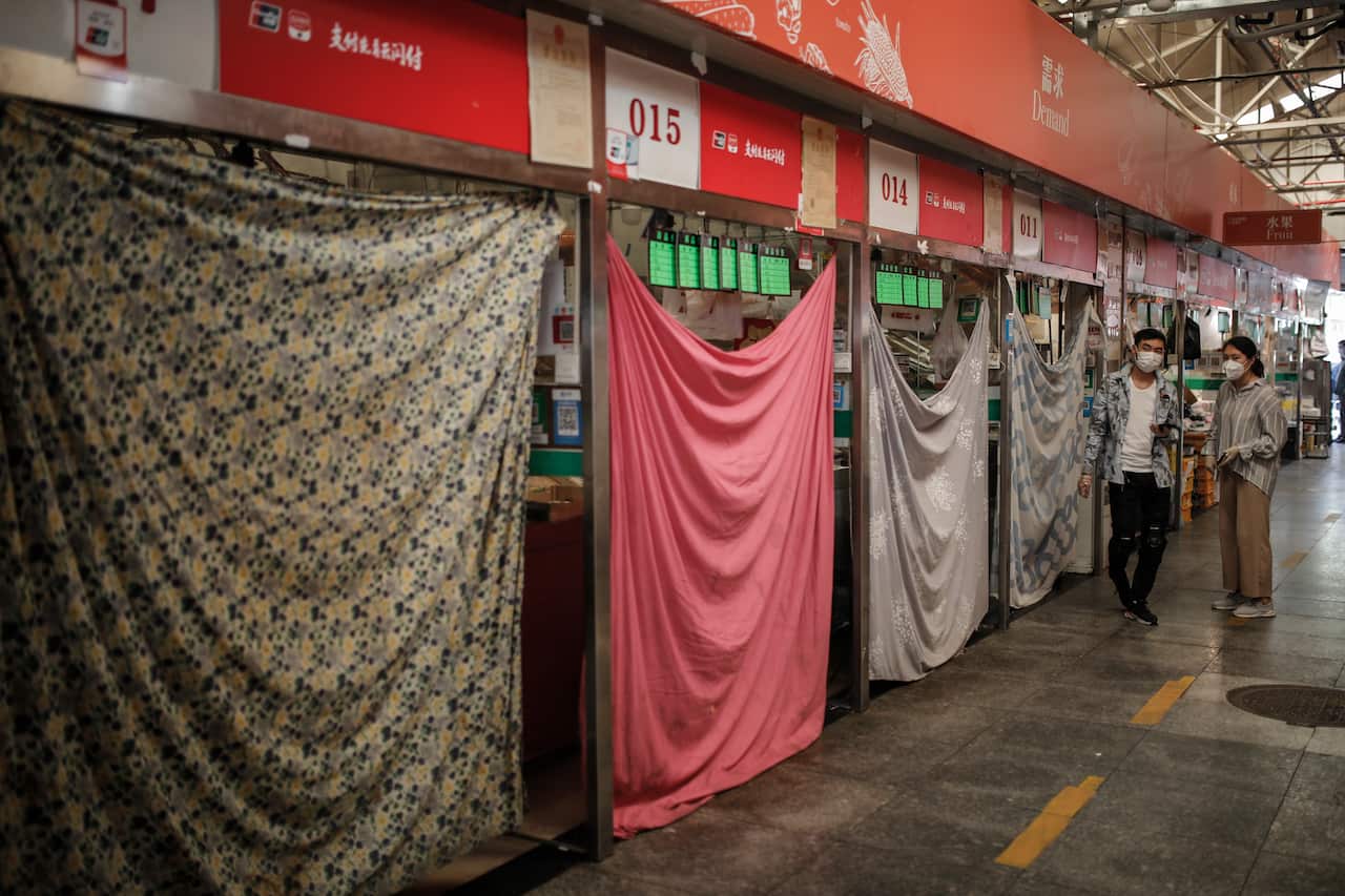 People wearing protective face masks stand beside many closed fruit stalls in a market in Beijing, China.