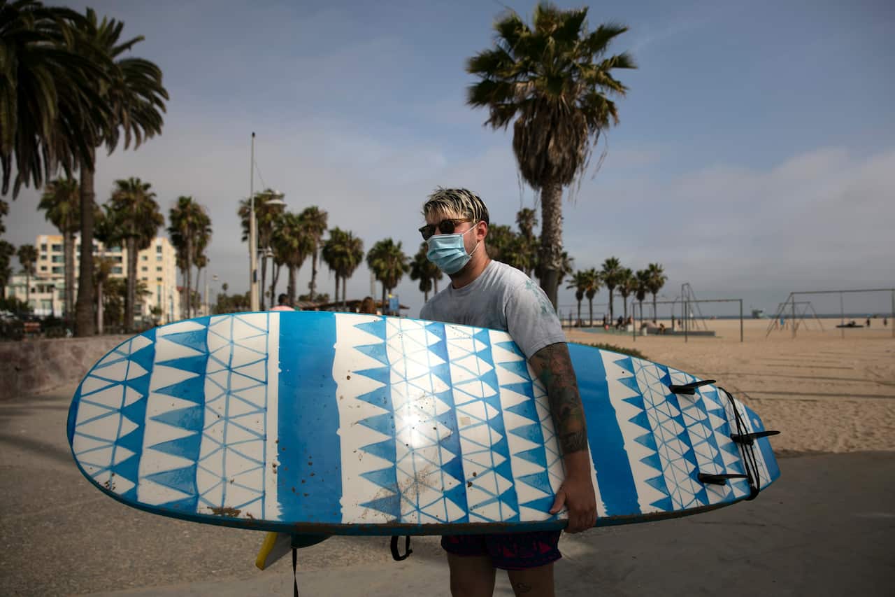 Joseph Carter, 27, carries a surfboard on the beach Tuesday, June 23, 2020, in Santa Monica, California.