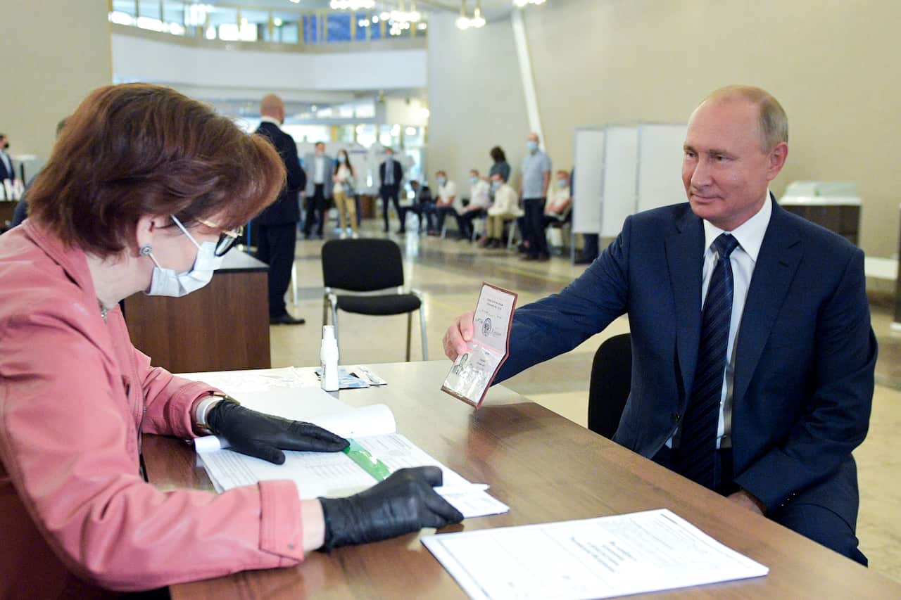 Russian President Vladimir Putin shows his passport to a member of an election commission as he arrives to take part in voting at a polling station in Moscow