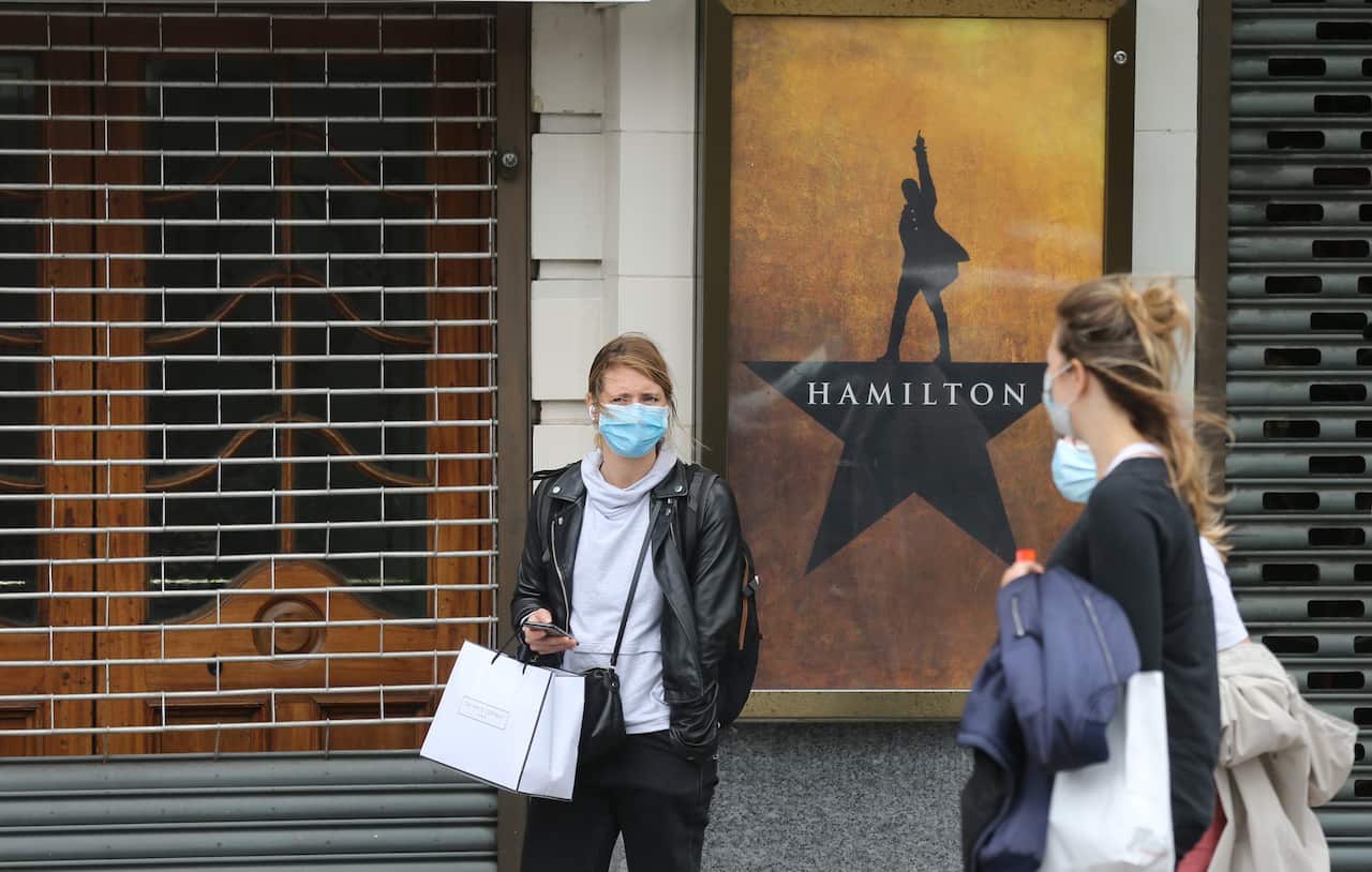 People wearing protective face masks walk past a closed-down Victoria Palace Theatre.