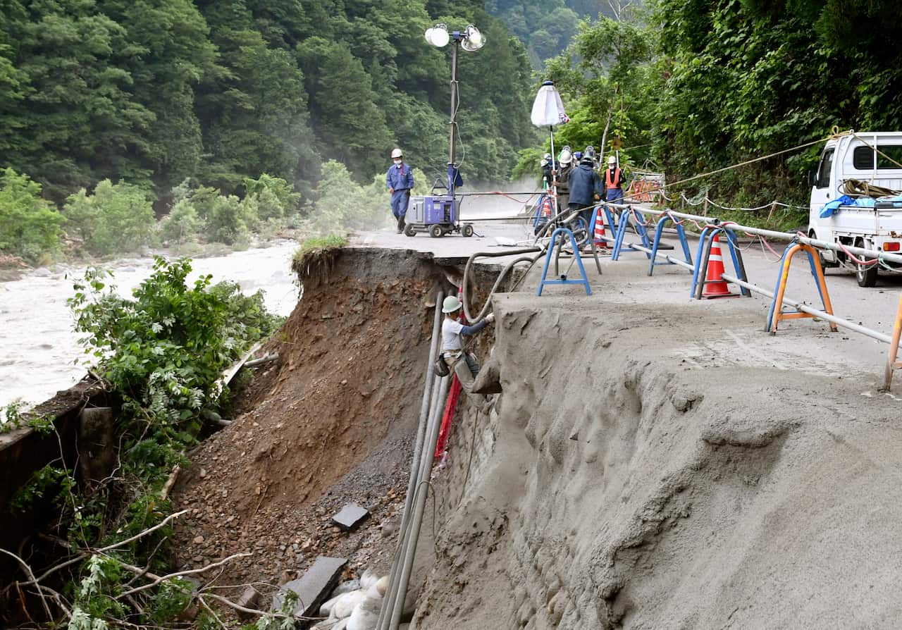 Workers attempt to restore a collapsed road as it was hit by heavy rains in Takayama, Gifu, southern Japan.