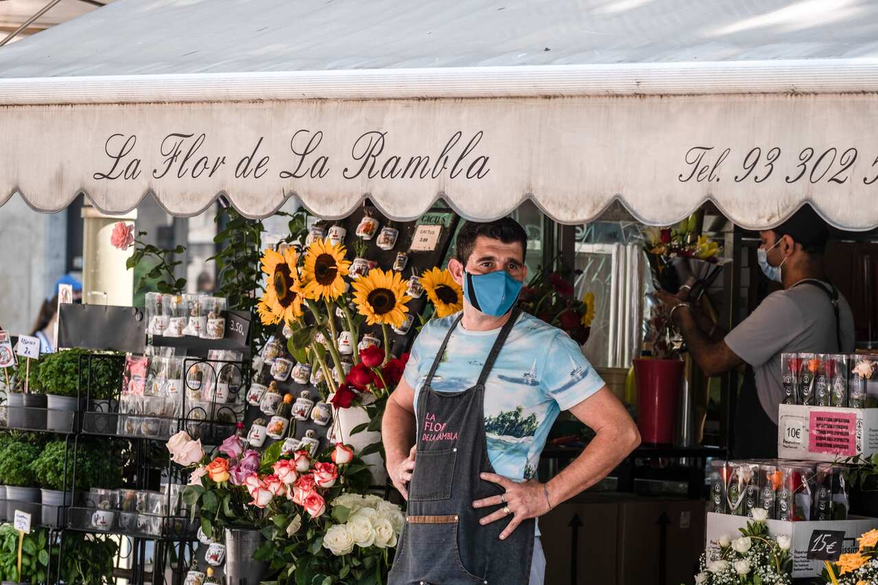 A shop assistant wearing a face mask is seen in one of the flower selling kiosks on La Rambla.
